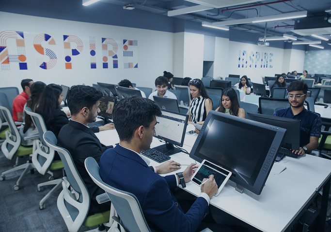 Student sketching a prototype on a tablet beside a pen display while classmates code in the lab