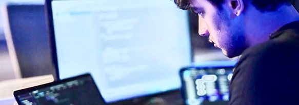 Student focused on code across multiple screens in a dimly lit lab