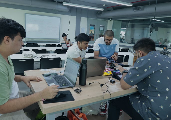 Students building prototypes on laptops and devices around a shared workbench